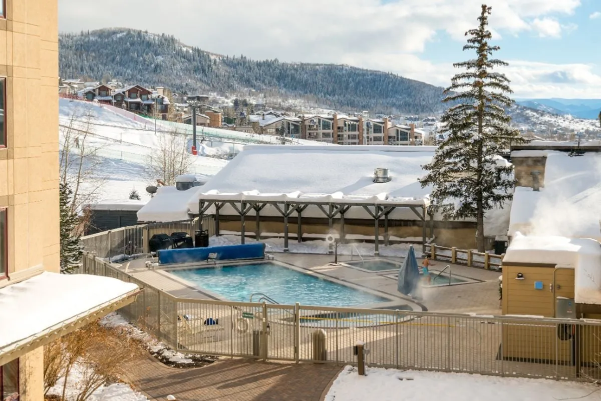 An exterior shot of the pool surrounded by a snowy landscape, with trees and mountains in the distance. The tranquil scene highlights year-round enjoyment, from cozy swims after skiing to peaceful sunset views.