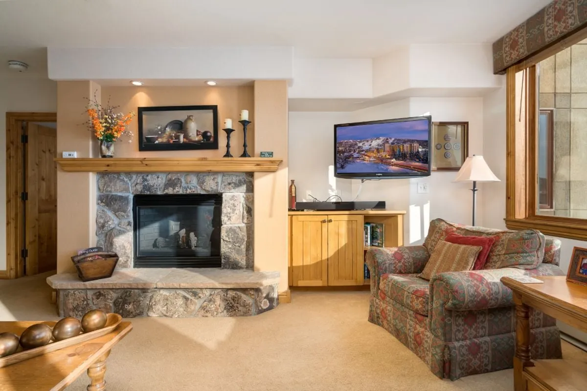 A cozy interior living area featuring a welcoming fireplace, comfortable armchairs, and wooden furniture. The scene suggests an inviting space for relaxing after a day out, either watching TV or socializing with friends.