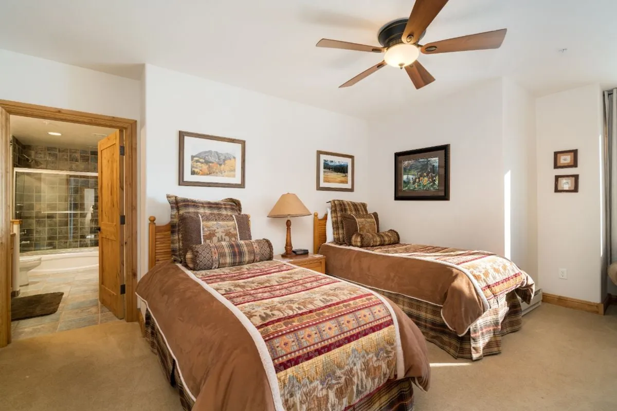 A cheerful bedroom setting with twin beds, patterned quilts, and morning sunlight streaming through the window. The wooden furnishings and soft lighting evoke a sense of relaxation and family bonding after a day spent exploring outdoors.
